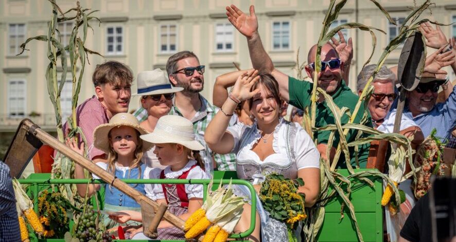 2025-09-07_EDF25_(c)ÖSF-Pöhlmann-1716 Menschen in Tracht und Alltagskleidung winken von einem geschmückten Erntewagen beim ernte.dank.festival. am Wiener Heldenplatz.