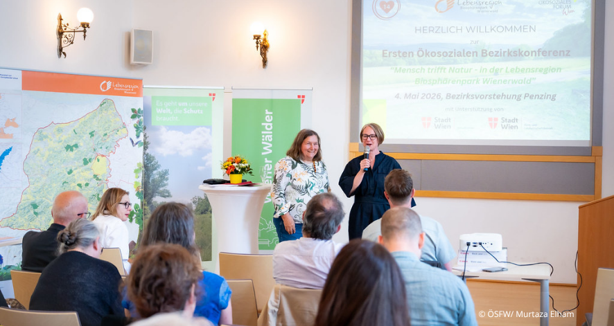 Ökosozoziales Forum Wien, Bezirkskonferenz 2025 Zwei Vortragende stehen vor Publikum bei der Ersten Ökosozialen Bezirkskonferenz in Wien. Im Hintergrund sind Informationsbanner und eine Präsentationsfolie zu sehen.