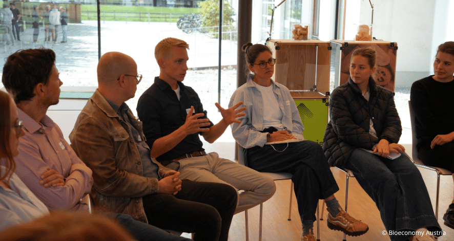 Bioeconomy Austria 1, BA, Workshop Kuchl, 2026 Ein Teilnehmer spricht gestikulierend in einer Diskussionsrunde des Bioeconomy-Austria-Workshops in Kuchl. Die anderen Teilnehmenden hören zu.
