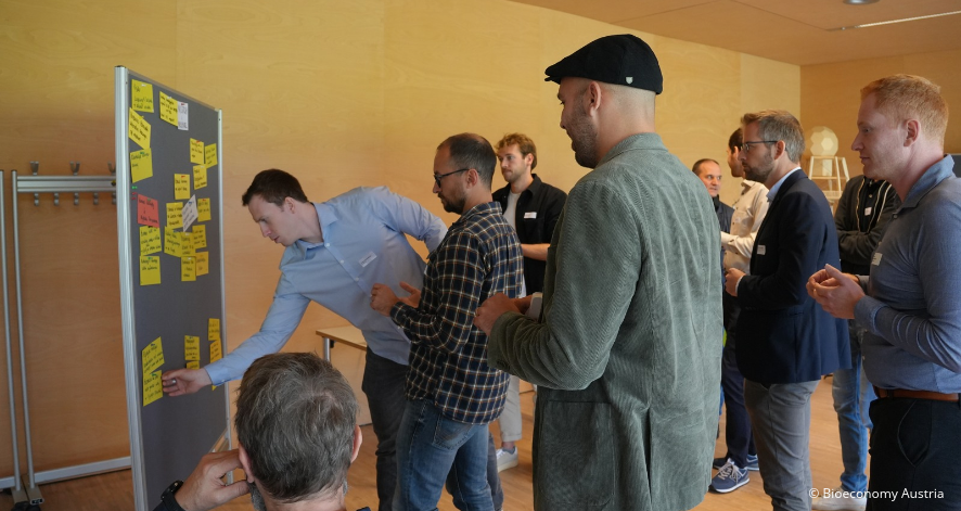 Bioeconomy Austria 3, BA, Workshop Kuchl, 2026, (c) Bioeconomy Austria Teilnehmende eines Bioeconomy-Austria-Workshops in Kuchl diskutieren und ordnen Haftnotizen mit Ideen und Ergebnissen an einer Pinnwand.
